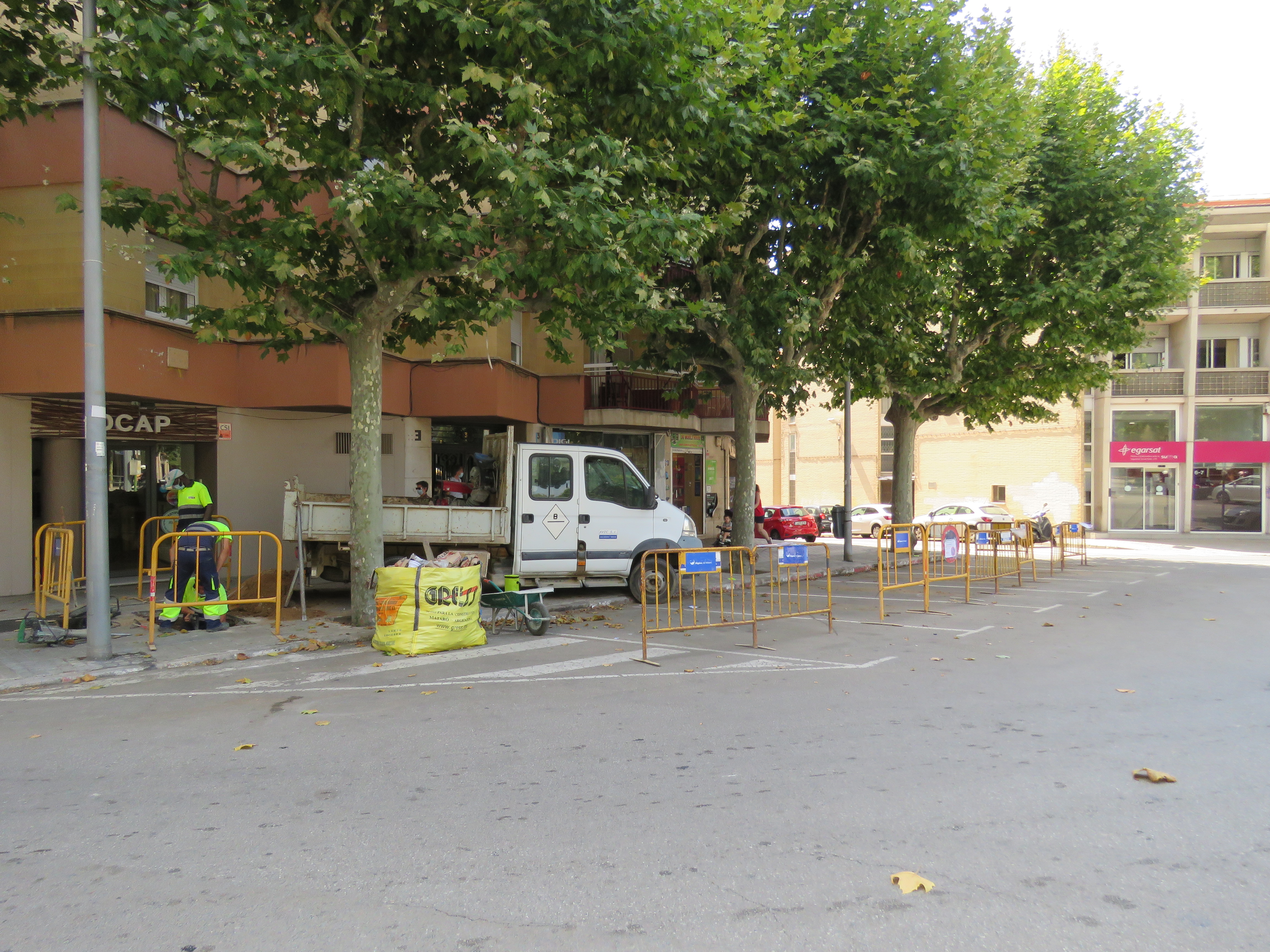 Obres al carrer de Mossèn Ramon Fornells. Tanques d'obres al costat de la vorera, operari treballant i furgoneta de manteniment aparcada rere les tanques. 