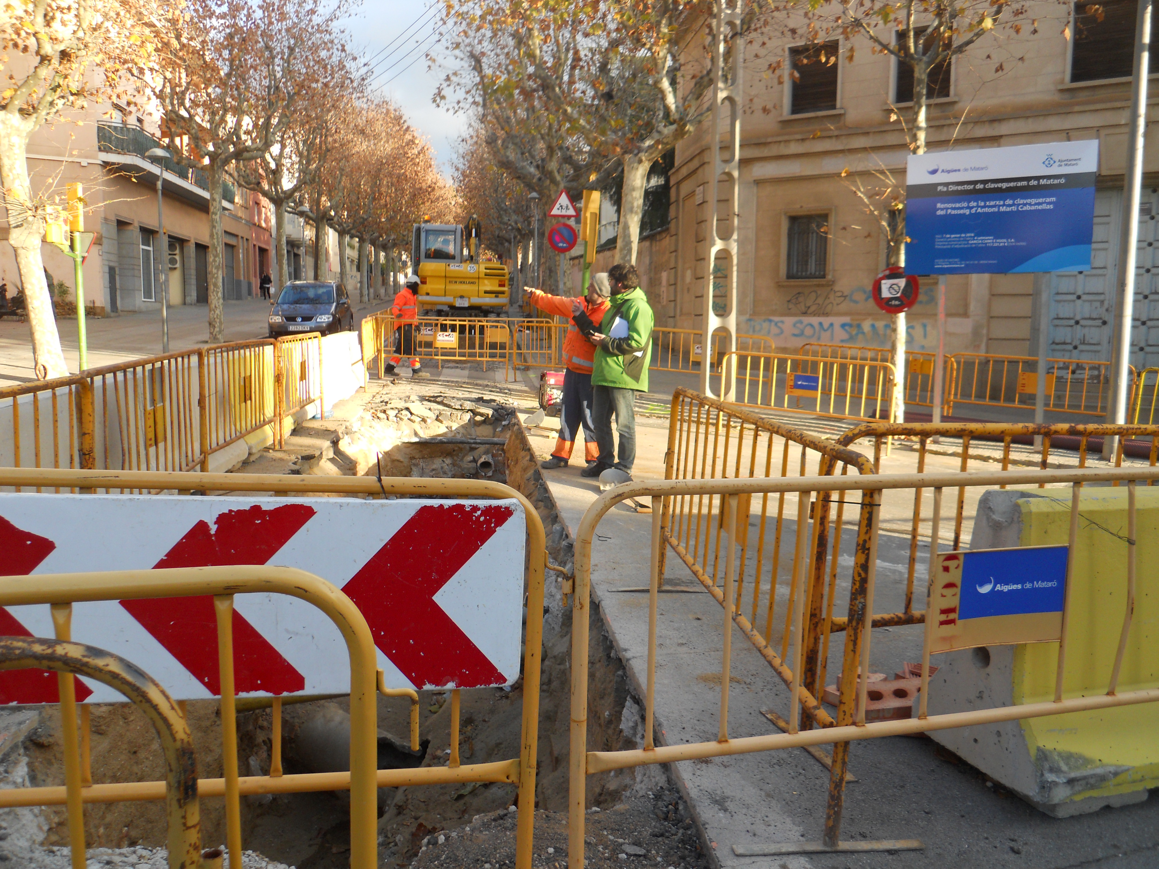 Dos treballadors davant d'unes tanques d'obra que protegeixen la rasa oberta al Passeig d'Antoni Cabanellas