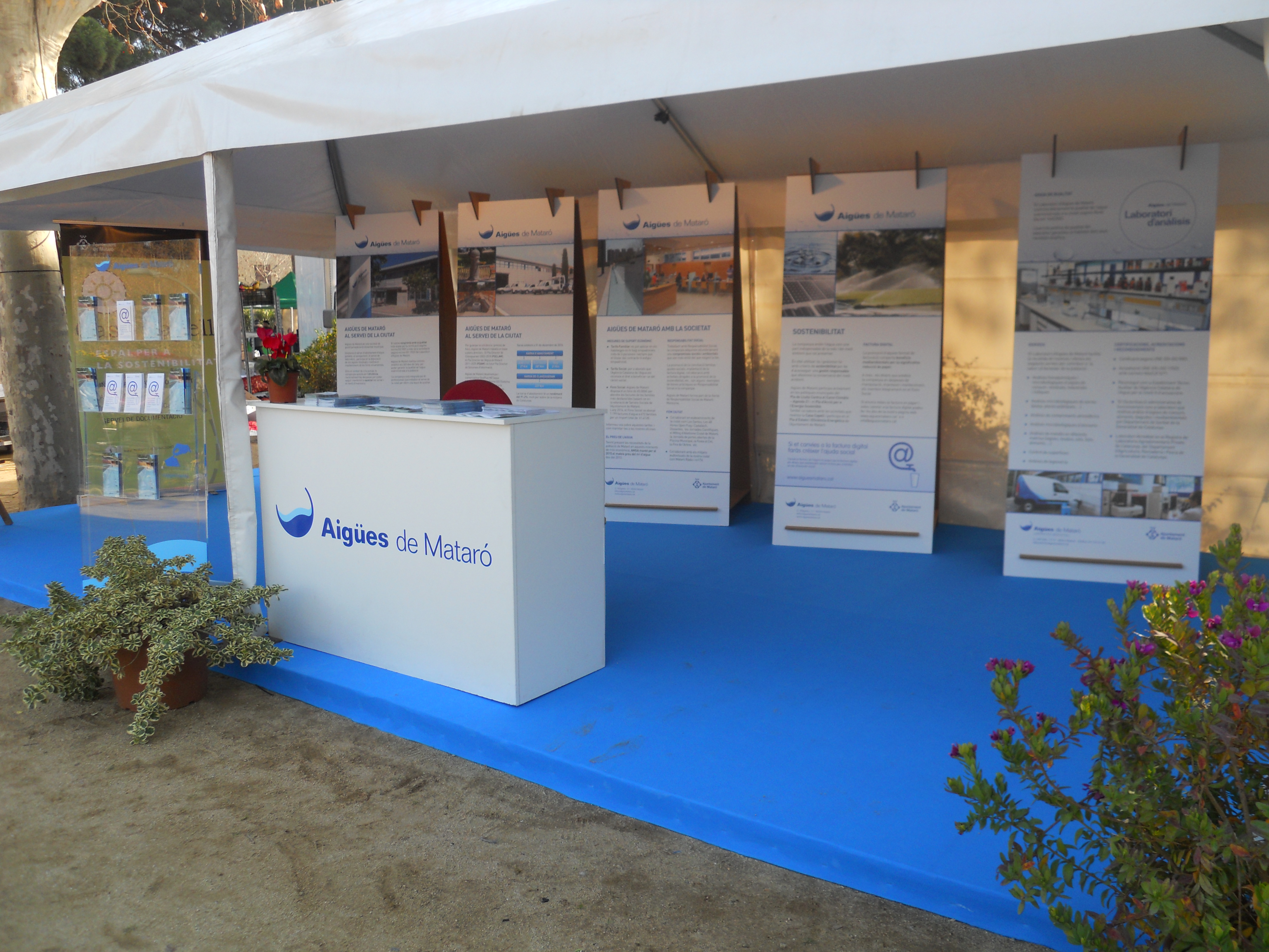 Interior de l'estand d'AMSA a la fira de la Natura, amb moqueta blava, un taulell amb logotip de la companyia i cartells explicatius al fons