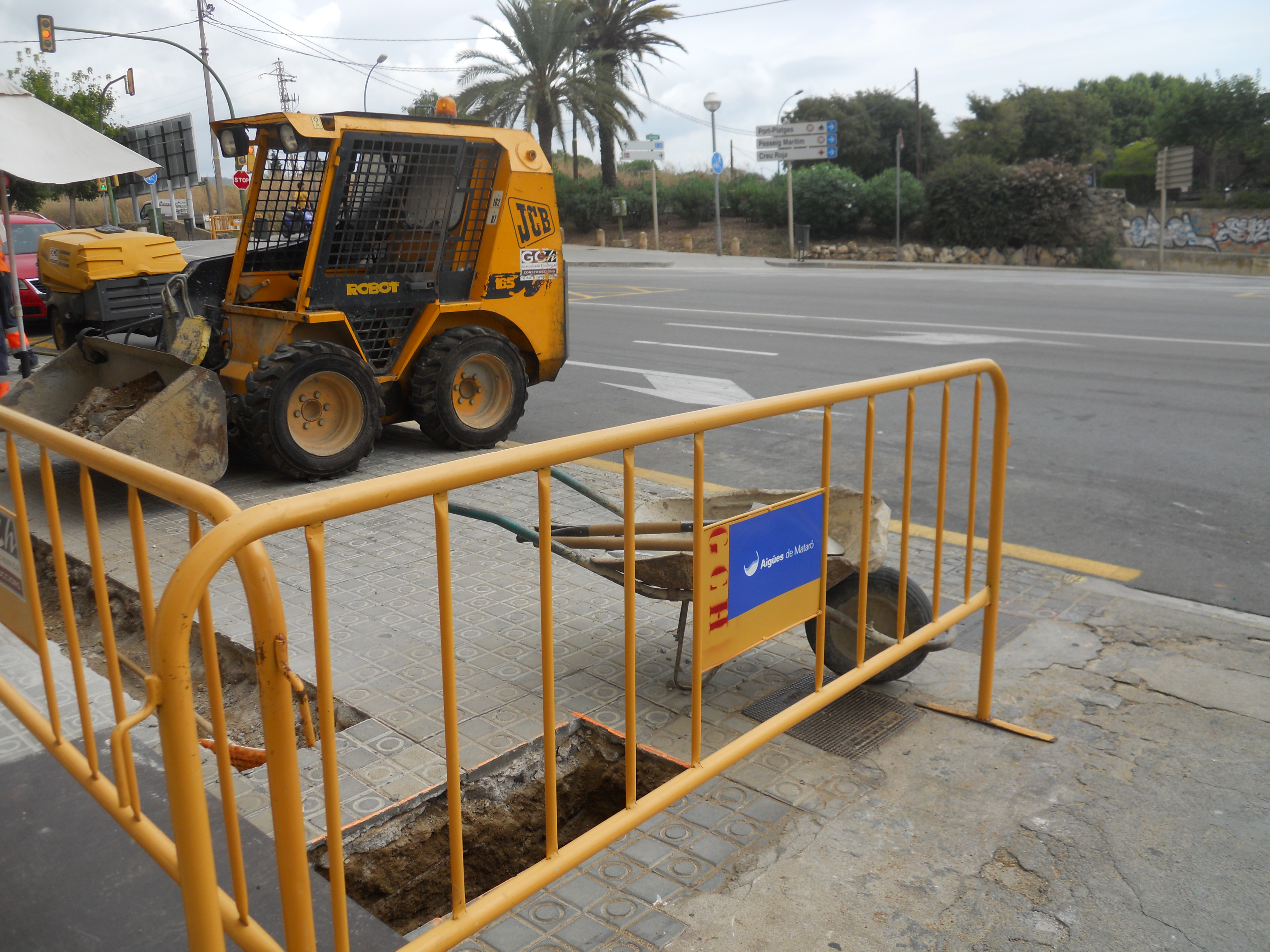 Imatge d'una excavadora al costat d'unes tanques d'obres que protegeixen dues rases.jpg