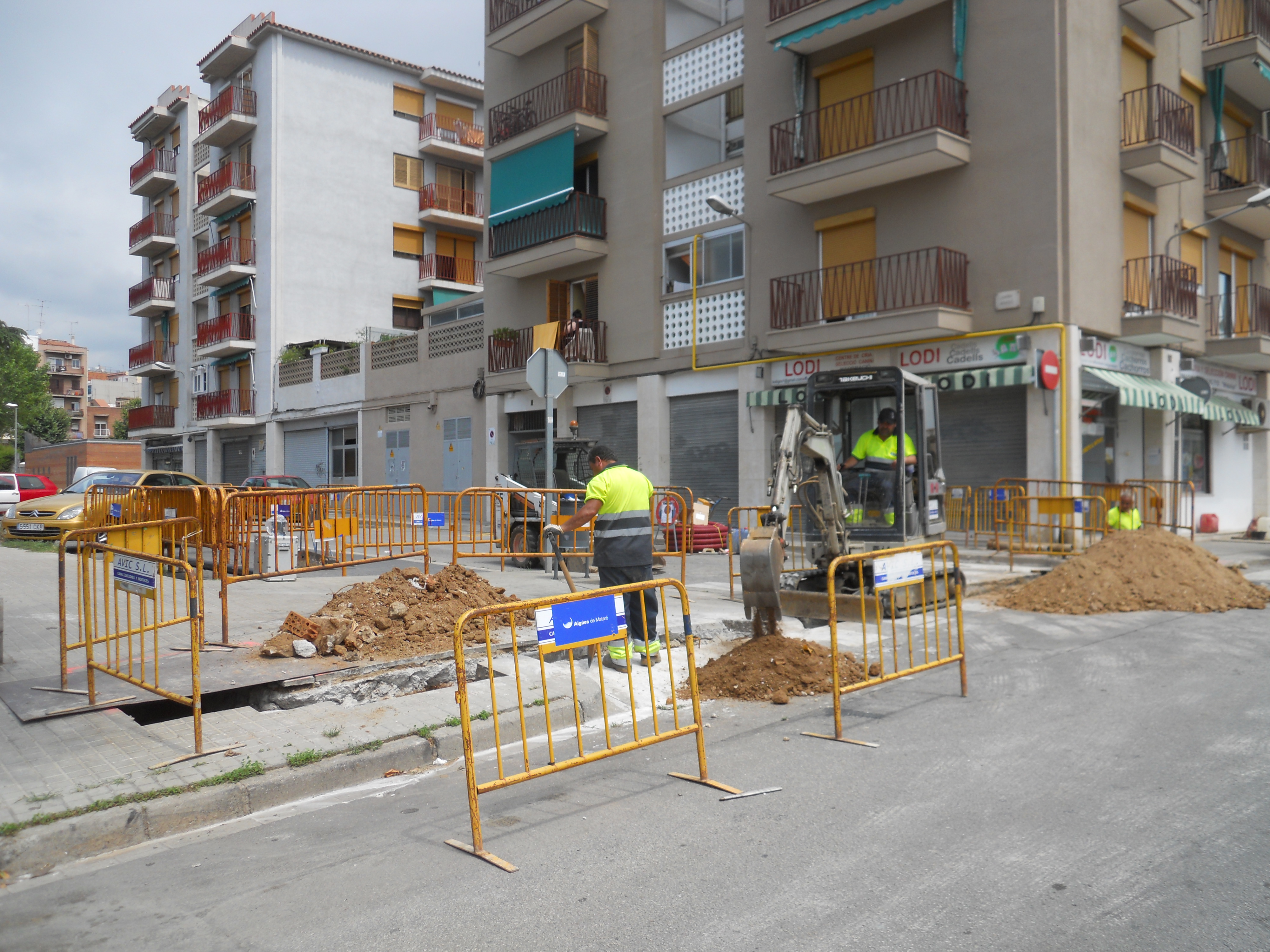 Operari obrint rasa al carrer de la Mataró i treballador operant una pala excavadora