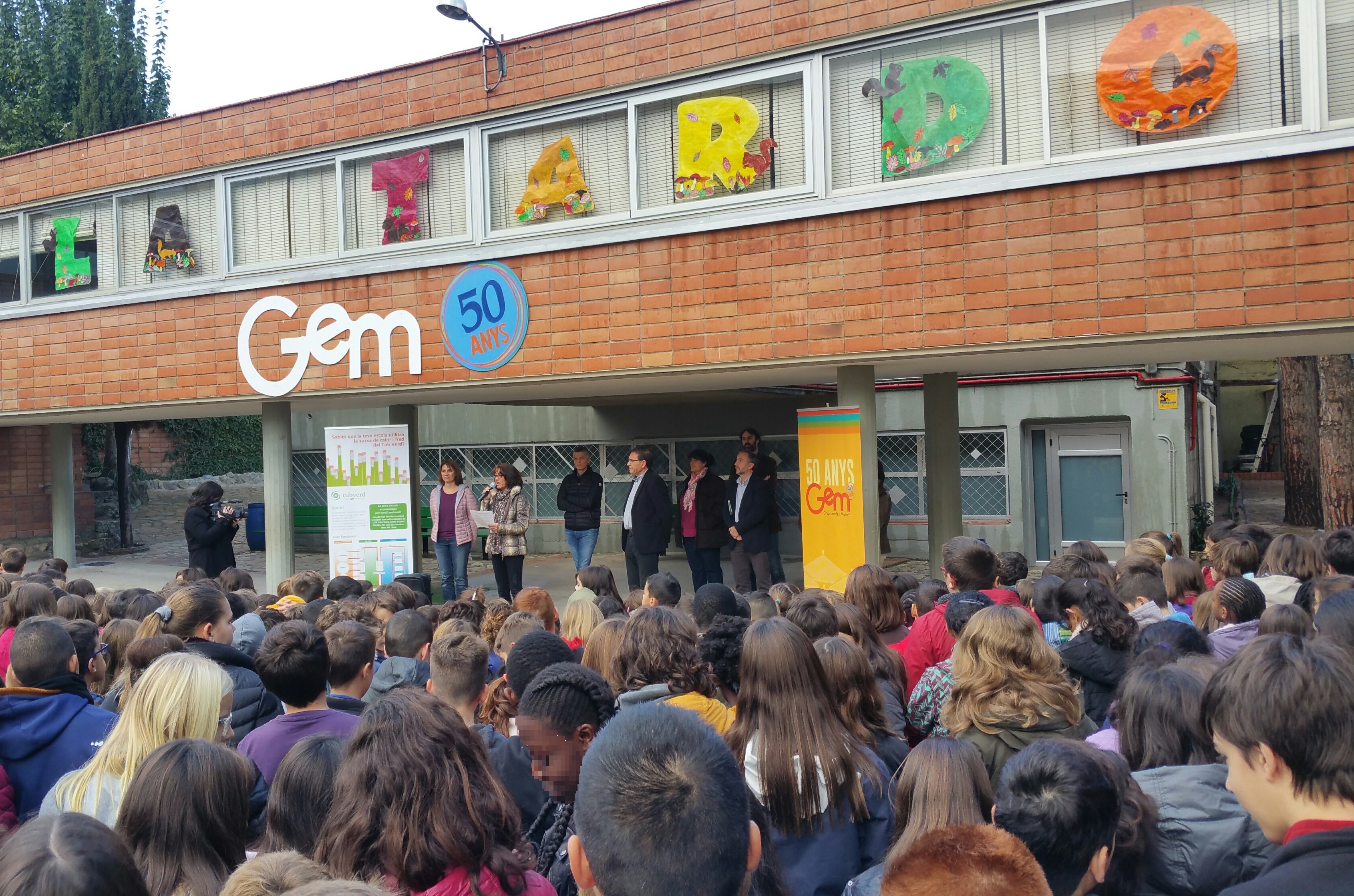 Entrada de l'escola GEM amb persones al davant escoltant parlament que fa la direcció de l'escola.jpg