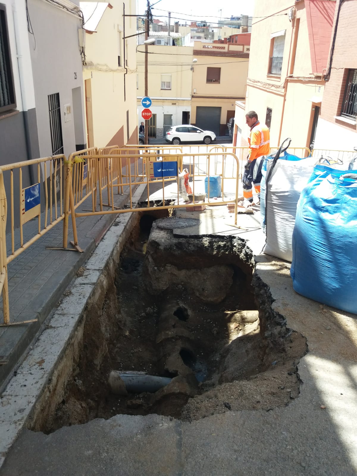 Rasa d'obres envoltada de tanques en primer pla amb tubs de clavegueram a la vista i operari controlant la rasa.jpg