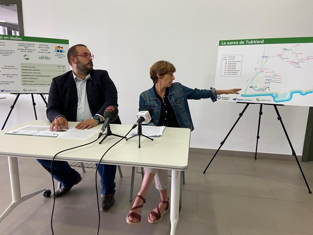 David Bote i Raquel Compta asseguts darrere d'una taula i assenyalant mapa de la xarxa de TubVerd, situat a la dreta