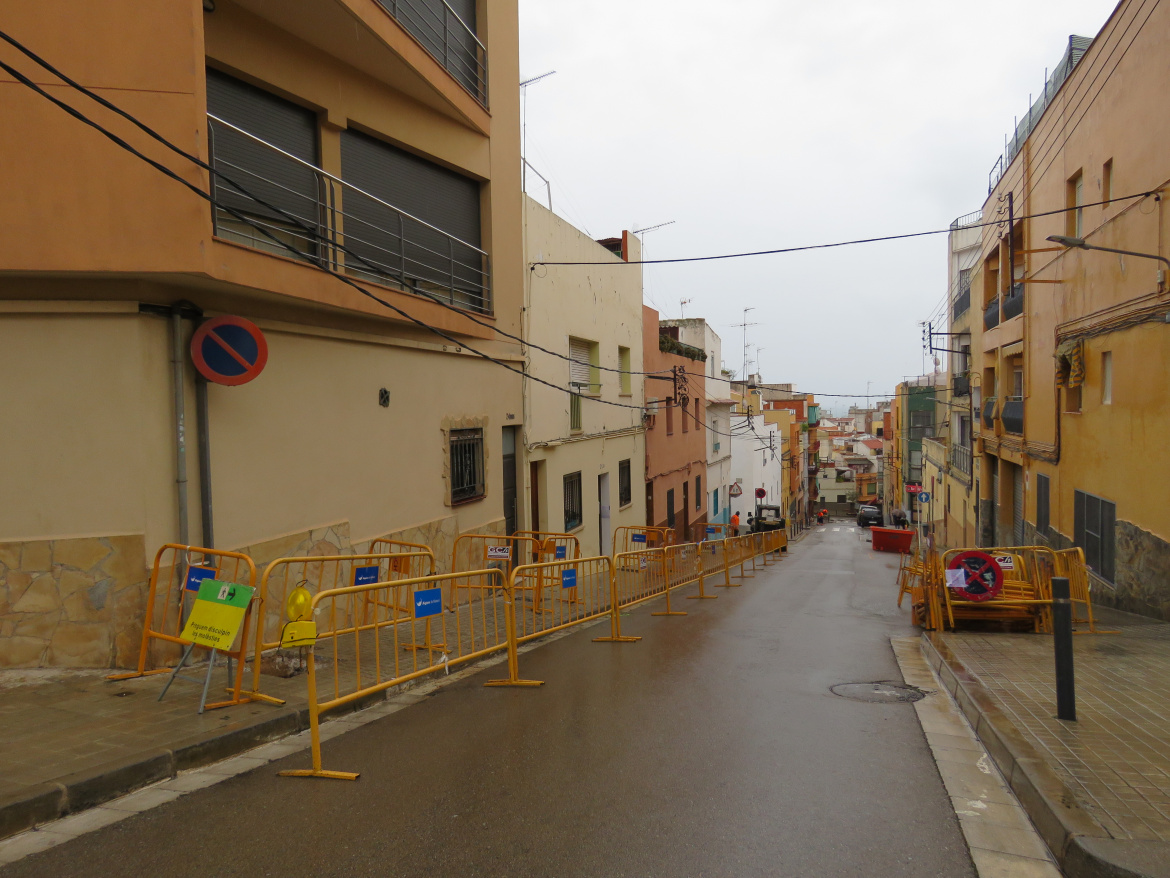 Imatge de carrer amb pendent i tanques d'obres protegint els laterals de la vorera