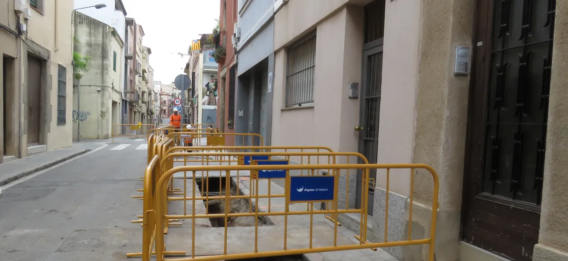 Rases obertes a l'asfalt del carrer de Sant ramon amb tanques que les protegeixen, al costat de les entrades d'uns habitatgesjpg