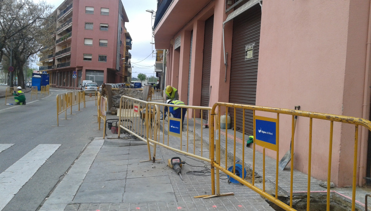Dos operaris d'Aigües de Mataró obrint una rasa amb una màquina, protegits per tanques d'obres