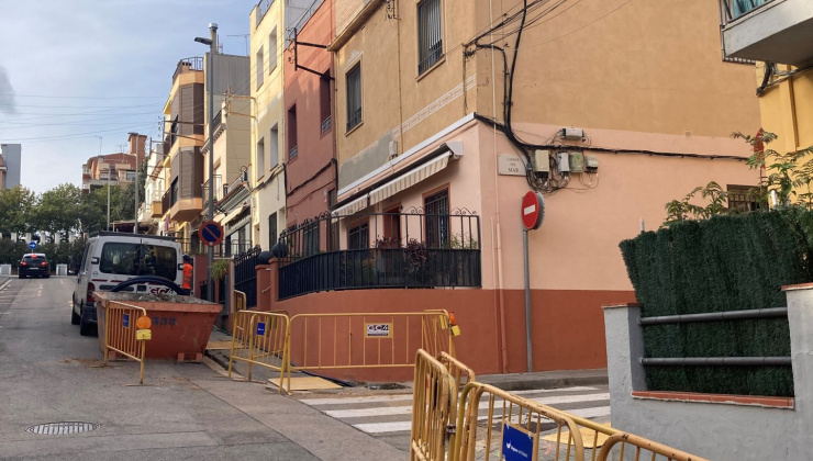 Carrer amb dues tanques d'obres en primer pla i contenidor d'obres 